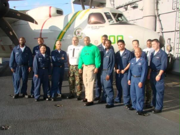 Ed DeJesus with the VAW-115 administrative department beside an E-2C Hawkeye aboard USS Kitty Hawk